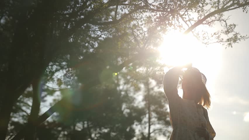 A woman is standing in front of a tree with the sun shining through the branches