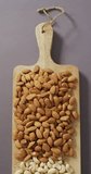 Vertical video of almond and cashew nuts piled on wooden chopping board with lilac background. healthy diet, food and nutrition.