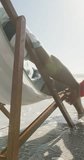 Vertical video of happy senior african american couple on sunbeds on sunny beach. spending free time at beach holiday.