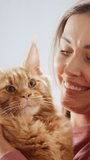 Vertical Screen: Close Up Portrait of an Attractive Young Woman Holding a Red Maine Coon Pet. Young Smiling Female Playing with the Cat. Owner Looking at Camera and Smiling