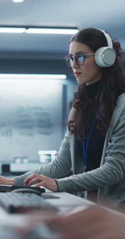 Vertical Screen: Portrait of a Young Engineer Working on Computer in a Technological Office Environment. Beautiful Multiethnic Woman Wearing Headphones, Writing Software Code for a Blockchain Project