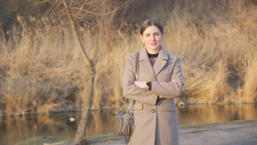 Attractive middle-aged woman in beige coat walks in park.