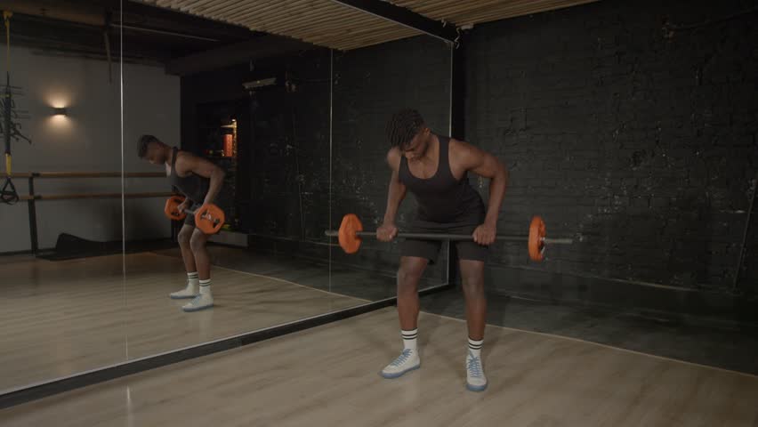 Active motivated sporty muscular build African man doing weightlifting training, practicing barbell row exercise , strengthening upper body and back muscles during indoor workout.