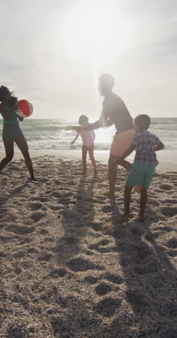 Vertical video of happy biracial family playing on sunny beach. healthy, active time beach holiday. Royalty-Free Stock Footage #3453700753
