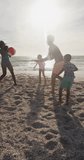 Vertical video of happy biracial family playing on sunny beach. healthy, active time beach holiday.