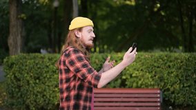 A young red-haired blogger walks through the park and writes a story for a social network or communicates with someone via video call on the go..