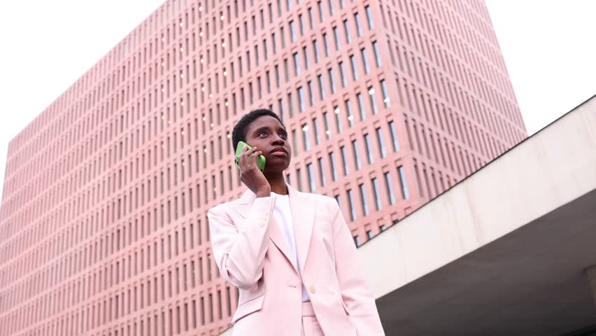 Young african businesswoman using a phone in finantial district. Young successful black businesswoman working in the street.