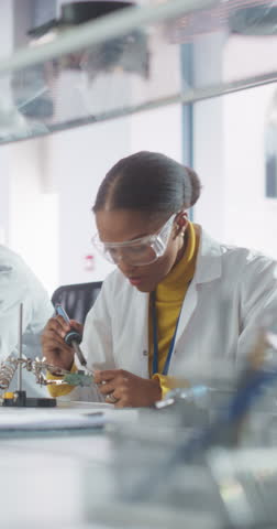 Vertical Screen: Diverse Team of Multiethnic Young Scientists Passing Internship in a Modern High Tech Laboratory. Cute African Female Working on Circuit Board with a Soldering Iron Royalty-Free Stock Footage #3453747717