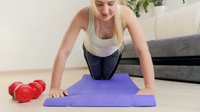 Slow motion video of beautiful young woman doing push ups on fitness mat at home