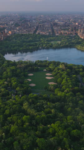 Vertical Screen: Aerial Helicopter Footage Over Central Park with Nature, Trees, People Having Picnic and Resting Around Manhattan Skyscrapers Cityscape. Beautiful Evening with Warm Sunset Light
