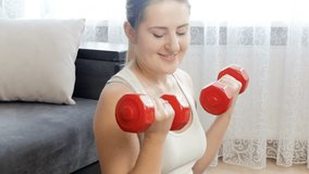 4k video of beautiful young woman lifting two red dumbbels at home