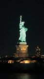 Vertical Screen: Aerial Fly-By Around the Statue of Liberty. Helicopter Footage of the Patriotic Monument in a Beautiful Night. Ferry Boats with Lights Transporting Tourists To and From Manhattan