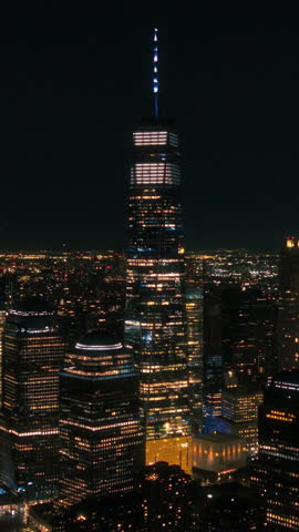 Vertical Screen: Night Aerial Footage of the One World Trade Center Skyscraper with Lights in Office Rooms Inside. Helicopter Making an Arc Shot Around the Building with a View on New York City