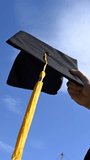 Close-up of a woman's hand with a graduation cap against the blue sky. Vertical video. 