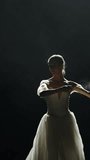 Dramatic dance, vertical video, elegant woman in a white tutu, ballerina dance and perform choreographic elements on a black background, using magnesia, haze effect on a dark stage.