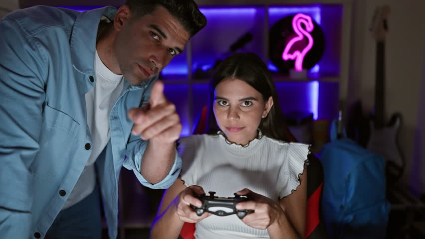 In a neon-lit home gaming room, a focused woman and assisting man engage in an intense video game session at night.