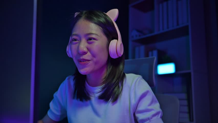 A female gamer is streaming a game for many people to watch, A young game streamer plays games on her computer in bedroom at home, A young woman is having fun playing a game.