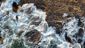 Beautiful slow motion video of wave crashing over rocks in the sunset. Top down drone footage of textured ocean movements.