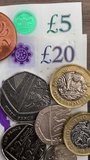 Vertical video – Macro closeup overhead shot of British sterling currency, with £5 and £20 notes, mixed denomination coins, and a finger adding penny coins.