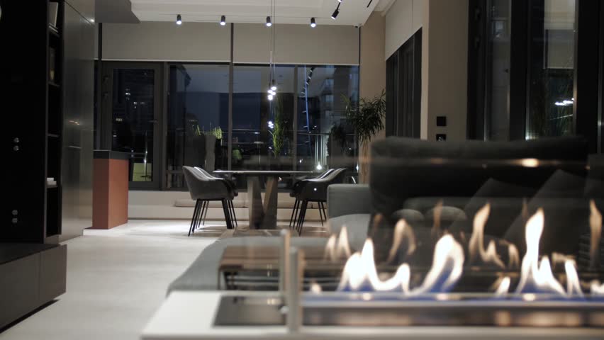 Modern fireplace with burning fire inside luxury apartment at night with light turned on. Minimalist interior in dark and black colors. Fire burning glowing inside mantelpiece. Royalty-Free Stock Footage #3453980291