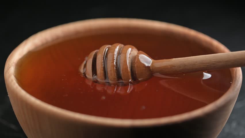 Natural organic honey dripping, pouring from wooden honey dipper close up. UHD 4k macro shot video