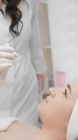 A young woman is lying on a couch in the office beautician who is performing botulinum injection procedure to reduce wrinkles around eyes and on face. Beautician makes markings on face for injections Royalty-Free Stock Footage #3454034861