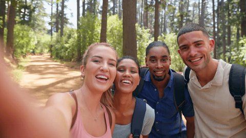 POV shot of young couple with friends wearing backpacks hiking along trail posing for selfie on mobile phone whilst walking in summer forest countryside - shot in slow motion Adlı Stok Video