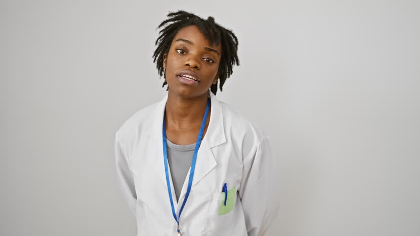 Worried young black woman in labcoat, her dreadlocks tucked away, a frown creasing her face. dealing with serious doubt, looking skeptic and unhappy. isolated against a stark white background. Royalty-Free Stock Footage #3454068503
