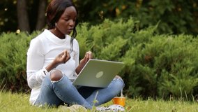 Angry shouting african american woman sitting on grass in city park gesturing talking video chat use laptop, chatting with friends, doing homework, distance working outside freelance online education
