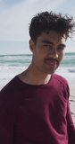 Vertical video of portrait of happy biracial man on sunny beach. healthy, active time beach holiday.