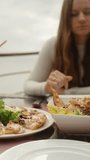 A young woman in a restaurant on a mountain by the sea, takes a slice of cucumber and croutons. Vertical video Social Media.