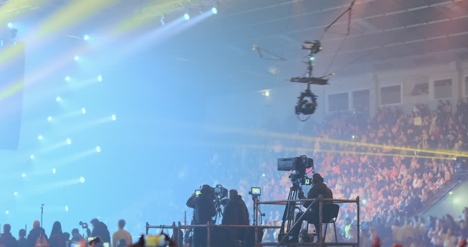 Professional filming of musical performance at live concert light. Videographers group film on platform, entertainment show event in spotlights equipment. Television broadcast, backstage production