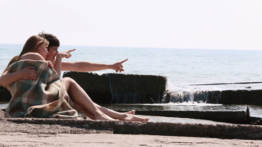 The lovely couple is spending the good time kissing and lying on the beach near the sea. They are wrapped in the knitted plaid.