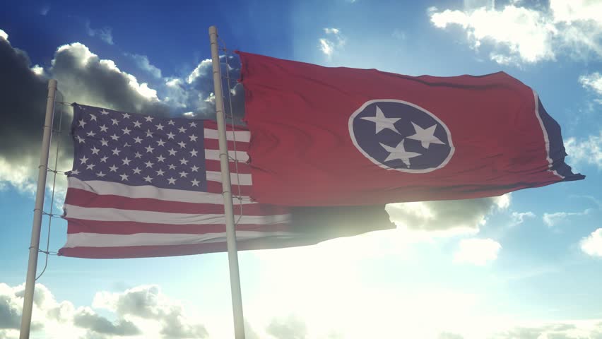 The Tennessee state flags waving along with the national flag of the United States of America. In the background there is a clear sky