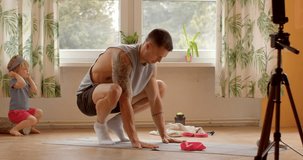 Young father video blogger demonstrates and performs physical exercises at home. Balance parenting responsibilities with maintaining a healthy lifestyle. Incorporating exercise into daily family life.
