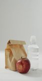 Vertical video of packed lunch in paper bag with apple and water on blue background. healthy diet, food and nutrition.
