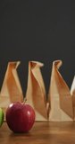 Vertical video of red and green apple with row of packed lunches in paper bags and grey background. healthy diet, food and nutrition.