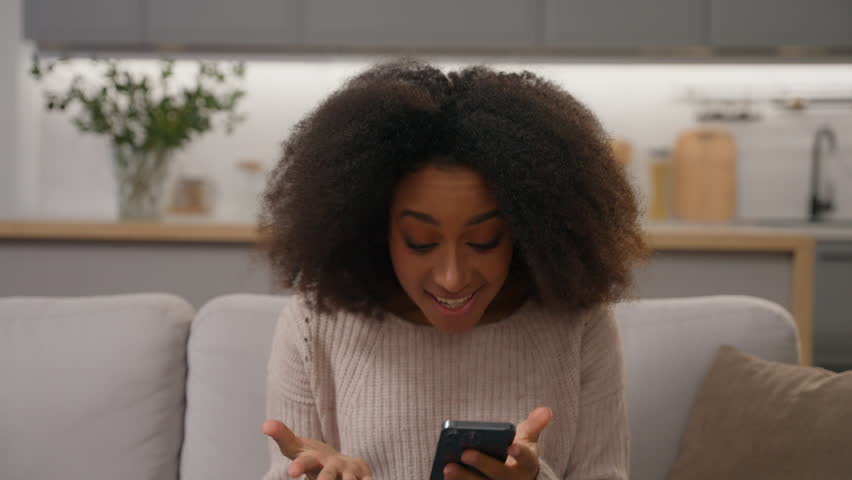 Shocked surprised African American woman joyful female looking at smartphone open mouth shock wonder happy emotion receive good news online win celebrate at home kitchen mobile phone app wow amazement Royalty-Free Stock Footage #3454219595