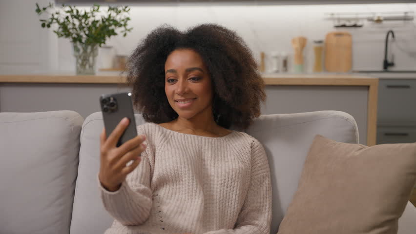 Happy smiling African american woman talking mobile phone smartphone online virtual meeting ethnic girl cheerful waving hand greeting record blog distant video call laughing with friends on home sofa Royalty-Free Stock Footage #3454220693