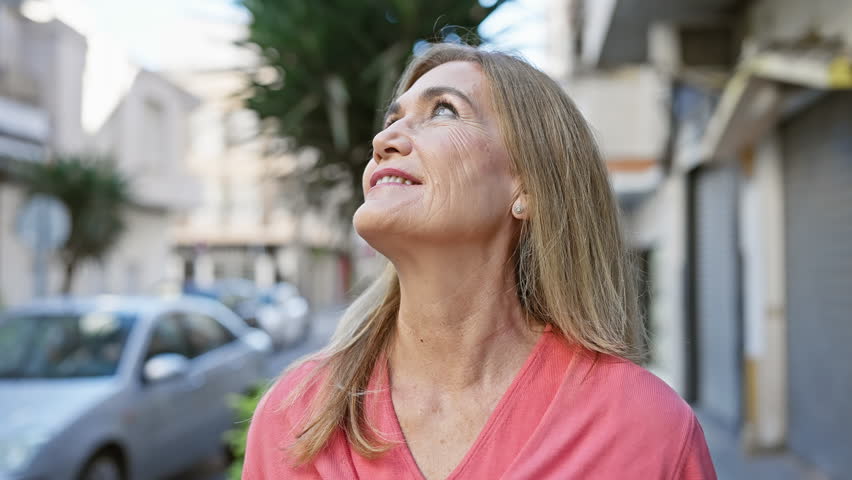 Mature woman smiling outdoors in urban settings, reflecting positivity in the city's everyday street life.
