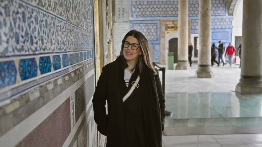 A smiling woman explores the historic topkapi palace in istanbul, surrounded by ancient tilework and architecture.