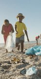 Vertical video of happy african american family segregating waste on sunny beach. spending free time at beach holiday.