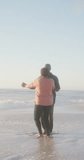 Vertical video of happy senior african american couple dancing on sunny beach. spending free time at beach holiday.
