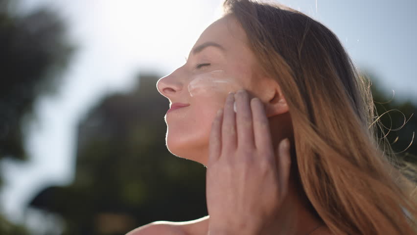 Close-up. The girl applies a white protective cream to her face with her hands and gently rubs it in while standing outdoors