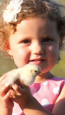 A little girl is holding a small chicken in her hands