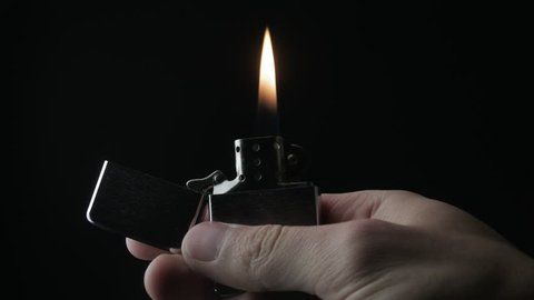 close-up of the opening and the burning of iron Zippo lighter on a black background