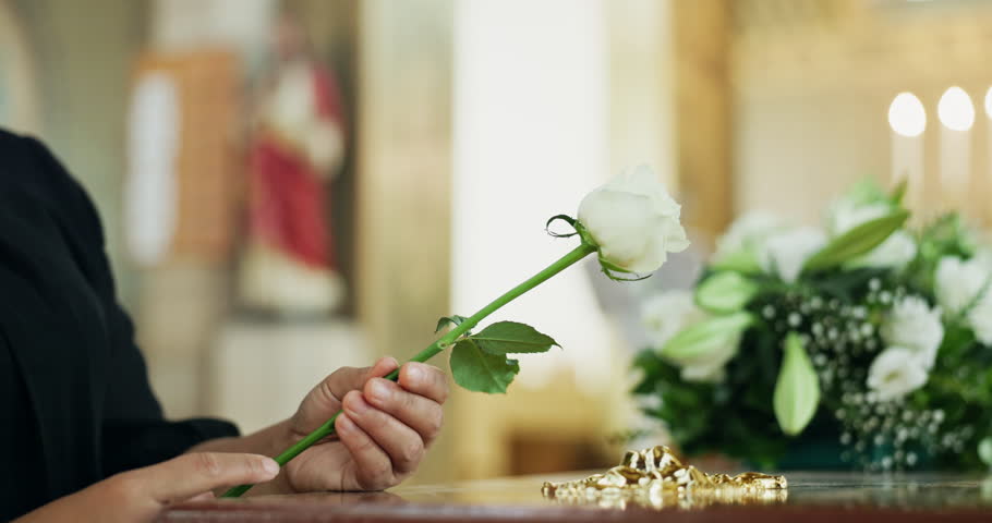 Grief, hand and person at coffin with flower at memorial service at church for respect, support and comfort. Death, funeral and widow with rose, memory and goodbye at casket for spiritual farewell.