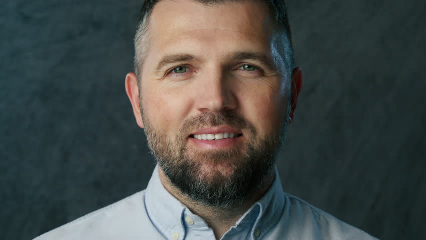 Positive smiling bearded man looking straight to camera and laughing with white teeth. Portrait 40s confident businessman in suit on grey background. Close up handsome middle age professional employee