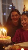 Vertical Screen: Happy Excited Girl Blowing Out Candles on a Delicious Birthday Cake. Young Happy Child is Surrounded by Her Family, Relatives and Friends, Sitting Behind a Table in a Cozy Living Room