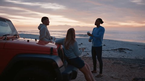 Young couple with friends on vacation standing by car at beach watching morning sunrise and drinking coffee on road trip  - shot in real time Video Stok